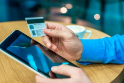 Imagem mostra apenas as mãos de um homem, uma segurando um cartão e a outra o celular, par tentar decidir o melhor banco digital