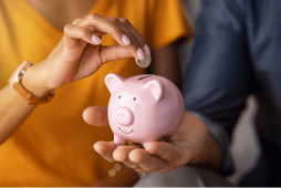 duas pessoas colocando uma moeda em um cofrinho para simbolizar como pagar menos tarifas bancárias