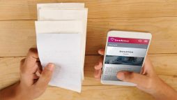 boletos em uma mão e o celular em outra- Como atualizar boleto Bradesco? Saiba tudo sobre o assunto!
