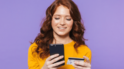 mulher ruiva segurando um cartão e crédito e um celular na outra mão- Canais de atendimento Nubank: saiba quais são eles