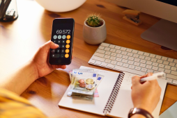 Pessoa calcula o Custo Efetivo Total no celular enquanto anota despesas em caderno, ao lado de dinheiro e computador.