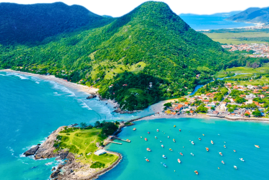 Vista aérea da Barra da Lagoa, em Florianópolis, com praias, morros verdes, casas e barcos no mar. Custo de vida em Florianópolis